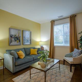 A cozy and modern living room with a yellow accent wall, stylish artwork, and comfortable seating.