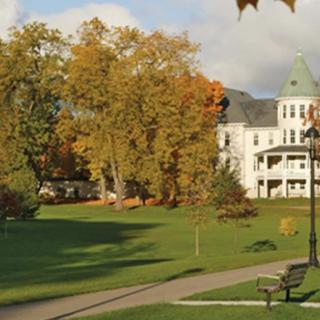 A scenic view of a campus with autumn foliage and a historic building in the background.