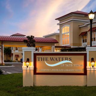 An elegant building entrance illuminated in the evening, featuring a prominent sign with 'The Waters' branding.