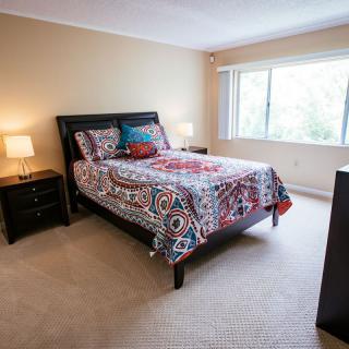 A cozy bedroom with a colorful bedspread, bedside lamps, and a large window.