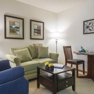 A cozy living room with a sofa, armchair, and coffee table, complemented by framed artwork and a floor lamp.