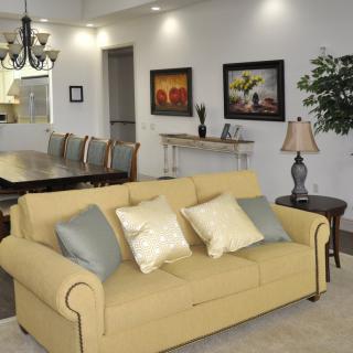 A cozy living room featuring a yellow sofa with decorative pillows, adjacent to a dining area with elegant chairs and wall art.