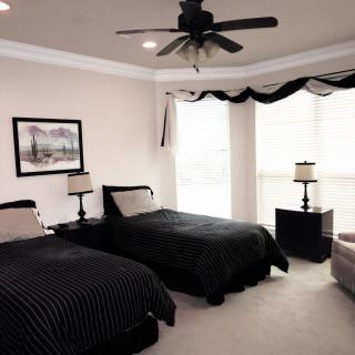 A modern bedroom with twin beds featuring black bedding, a ceiling fan, and ample natural light.