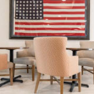 A seating area with chairs and tables is set against a backdrop of a framed American flag.