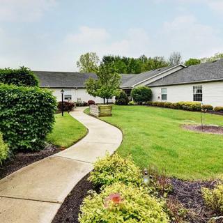 A curved pathway leading through a well-maintained garden with lush greenery and low buildings in the background.