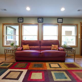 A cozy living room featuring a red sofa, colorful geometric rug, and large windows.