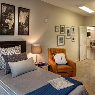 A modern and cozy bedroom featuring a neatly made bed, an orange armchair, and decorative artwork on the walls.