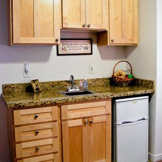 A compact kitchenette with wooden cabinets, granite countertop, and a mini fridge.