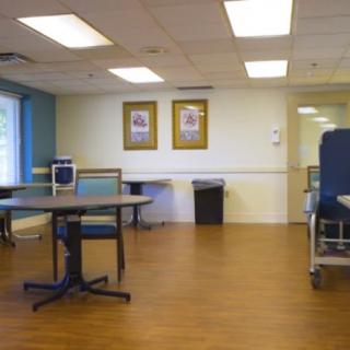 An empty hospital waiting room with chairs and tables, featuring wooden flooring and artwork on the walls.