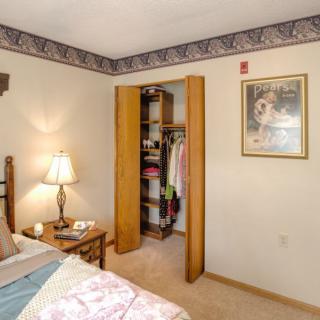 A cozy bedroom with an open closet, a bedside table with a lamp, and a painting on the wall.