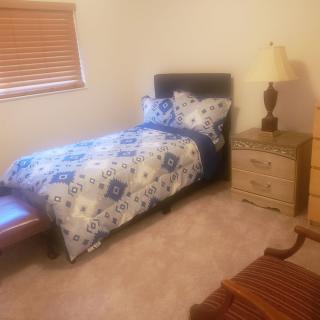 A cozy bedroom featuring a single bed with floral bedding, a wooden nightstand with a lamp, and carpeted flooring.