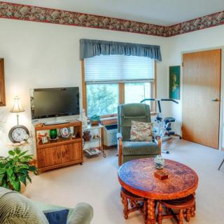 A cozy living room with a television, chairs, and a wooden table by the window.