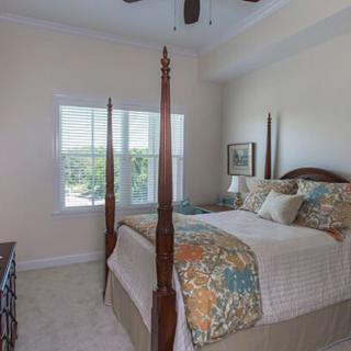A cozy bedroom with a four-poster bed, featuring colorful bedding and pillows, complemented by a large window letting in natural light.