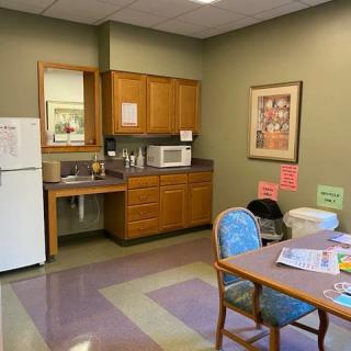 A small break room with a kitchenette, including a refrigerator and microwave, alongside a dining table and chairs.