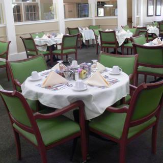 A neatly set dining table with green chairs in a restaurant.