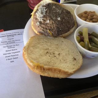 A meal consisting of a burger, baked beans, and green beans on a plate.