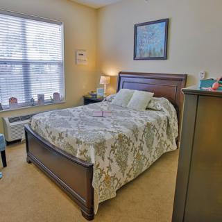 A cozy bedroom with a large bed, bedside lamp, and bright window.