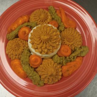 A colorful gourmet dish featuring artfully arranged vegetables and other ingredients on a red plate.