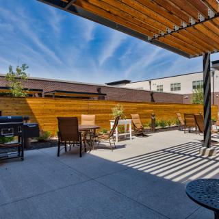 A sunny patio with a pergola, featuring outdoor seating and wooden fencing.