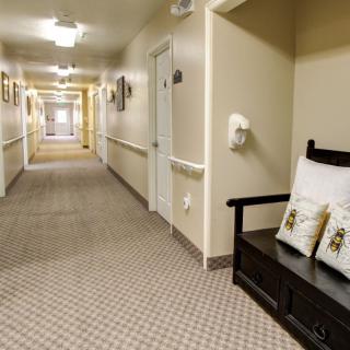A long, carpeted hallway with a bench and decorative pillows along the wall.