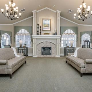 Elegant living room with a central fireplace and stylish chandeliers, featuring sofas and arched windows.