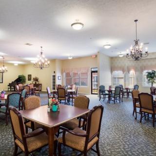 A spacious and well-lit dining room featuring multiple tables and chairs with elegant chandeliers.
