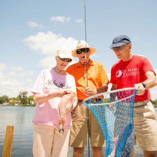 Three people standing by a lake holding a fishing net on a sunny day.