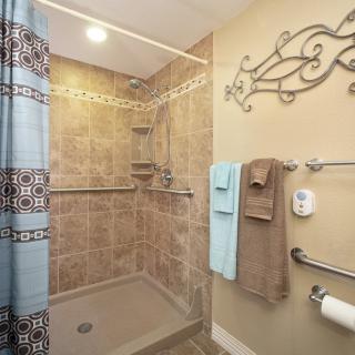A well-designed bathroom featuring a tiled walk-in shower with grab bars and neatly hung towels.