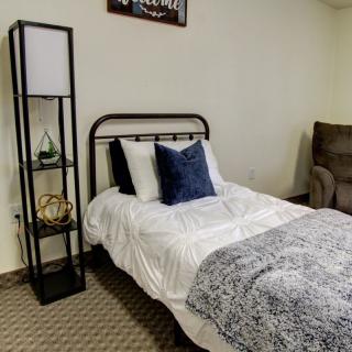 A cozy bedroom featuring a single bed with white bedding and a blue pillow, complemented by a black metal frame and a nearby floor lamp.