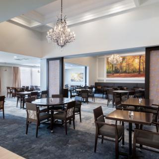 An elegant dining area featuring a chandelier, artwork, and neatly arranged tables and chairs.