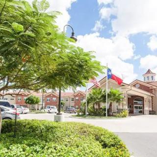 A view of a building with flags displayed in front, surrounded by trees and shrubs on a partly cloudy day.