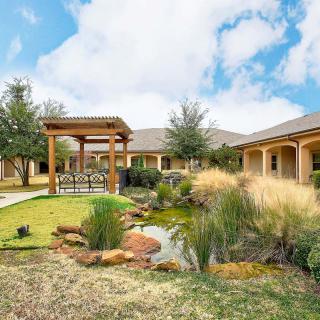 A courtyard featuring a landscaped garden with a pond, surrounded by buildings under a bright blue sky.