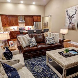 A modern living room with an open kitchen layout, featuring a leather sofa, armchairs, and elegant artwork.
