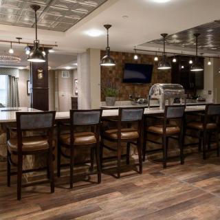 A modern bar interior with a long counter and high stools, complemented by warm lighting and wood flooring.
