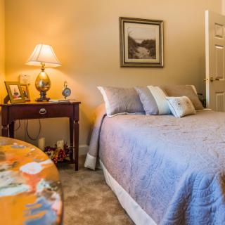A cozy bedroom featuring a neatly made bed, a warm lamp on the nightstand, and tasteful decor.