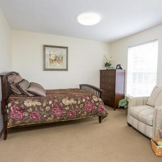 A cozy bedroom with a bed, dresser, and armchair near a window.
