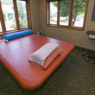 A therapy room equipped with a large exercise mat and windows providing natural light.