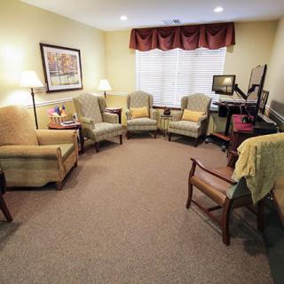 A cozy living room with several chairs arranged in a circular formation, featuring soft lighting and artwork on the walls.