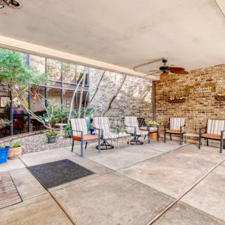 A cozy outdoor patio with seating and stone walls, featuring plants and a covered area.
