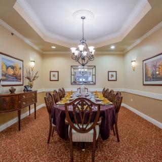 An elegant dining room with a long formal table, chandelier, and artwork on the walls.