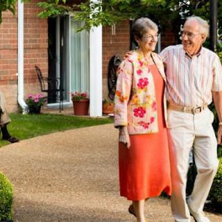 An elderly couple taking a stroll through a garden outside a retirement home.