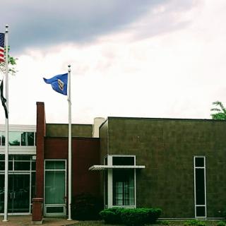 A modern building displaying various flags against a cloudy sky.