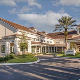 A sunny view of a residential building with palm trees and a driveway.