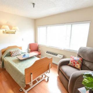 A well-lit hospital room featuring a bed, chairs, and large windows.