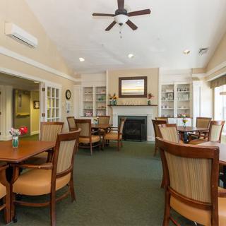A cozy dining area with multiple tables and chairs, featuring a fireplace and ceiling fan.
