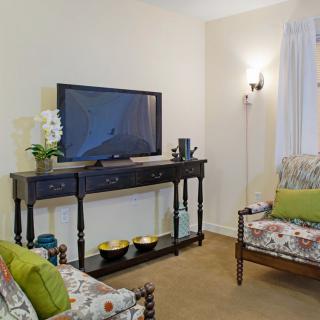 A cozy living room with a television on a console table, accompanied by floral sofas and tasteful decor.