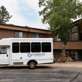 A shuttle bus parked outside a building surrounded by trees.