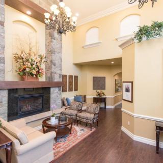 A spacious living room with a high ceiling, featuring a fireplace and elegant chandelier.