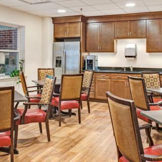 A modern dining area with wooden chairs and tables, featuring a kitchen setup with stainless steel appliances.