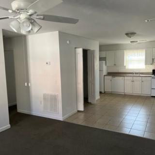 A view of a living room and kitchen area in an open-plan layout, featuring a ceiling fan and white cabinetry.